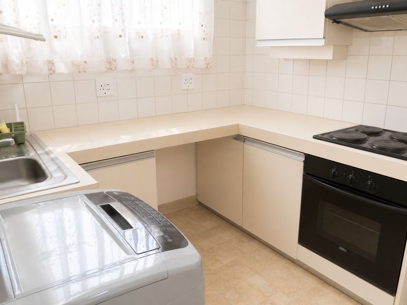 A functional kitchen featuring built-in cabinetry, laminate countertops, a stainless steel sink, and integrated cooking appliances including an oven and hob.