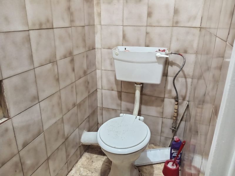 A small bathroom featuring a basic toilet and dated wall tiling, currently in need of renovation and cosmetic updates.