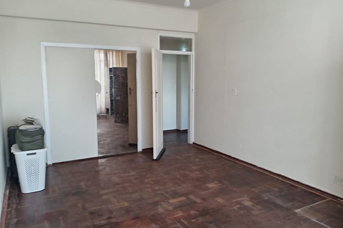 An empty bedroom featuring original parquet flooring, a built-in cupboard, and a transom window above the doorway, offering a blank canvas for renovation.