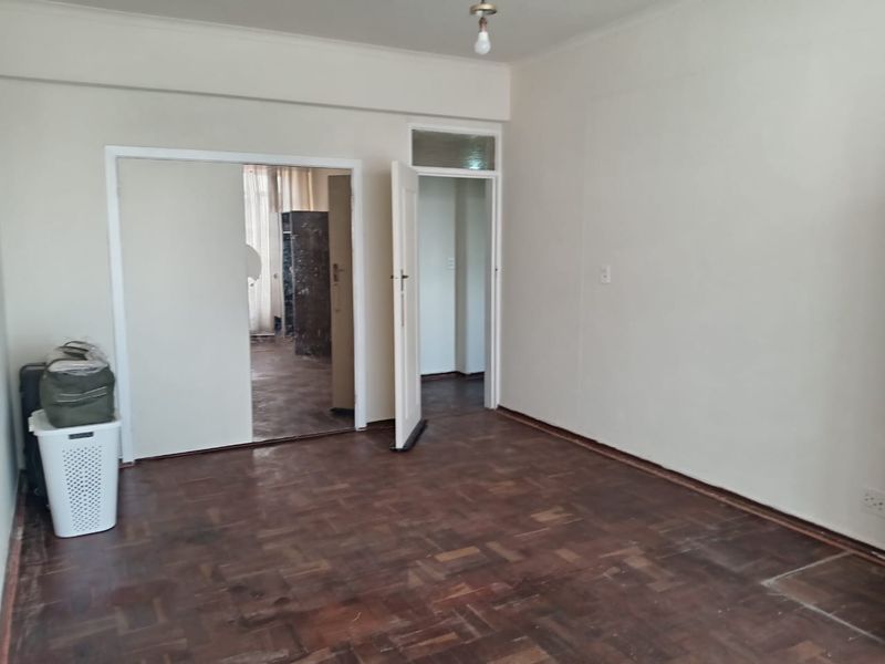 An empty bedroom featuring original parquet flooring, a built-in cupboard, and a transom window above the doorway, offering a blank canvas for renovation.