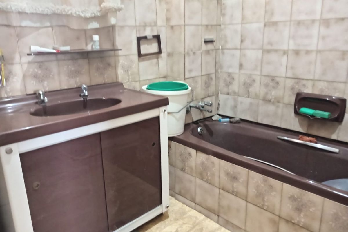 A dated bathroom featuring brown vanity cabinetry, a matching bathtub, and patterned wall tiles in need of modernization.