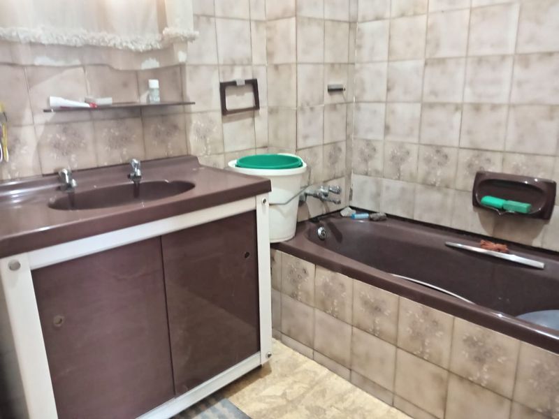 A dated bathroom featuring brown vanity cabinetry, a matching bathtub, and patterned wall tiles in need of modernization.