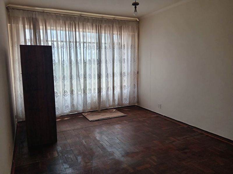 An empty bedroom featuring original parquet flooring and large windows with existing curtain tracks, offering a blank canvas for renovation.