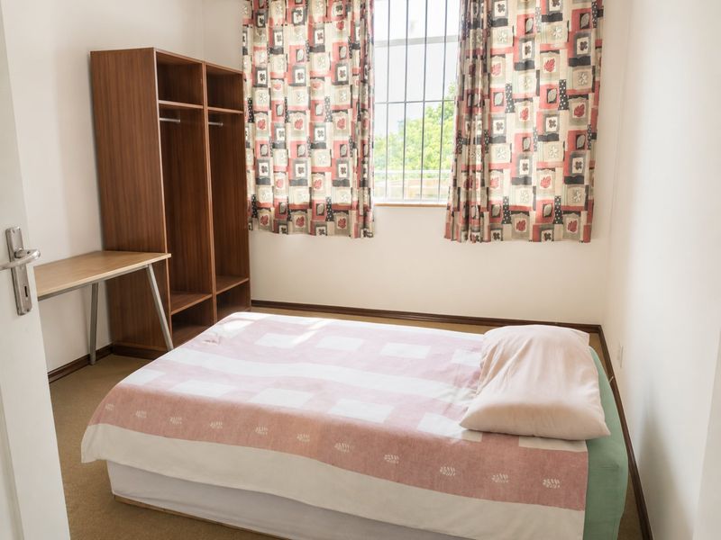 A functional bedroom featuring carpet flooring, security bars on the window, and neutral wall finishes.