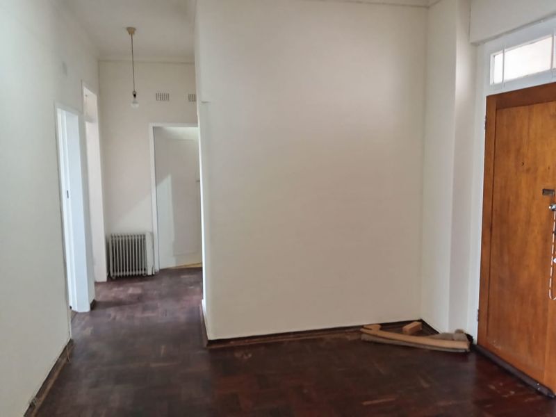 An empty entrance hall featuring dark parquet flooring, a solid timber front door, and a wall-mounted radiator.