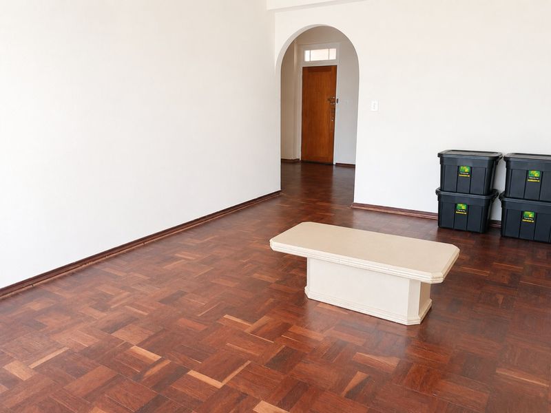 An empty living room featuring classic parquet timber flooring and an elegant arched doorway leading to the entrance.