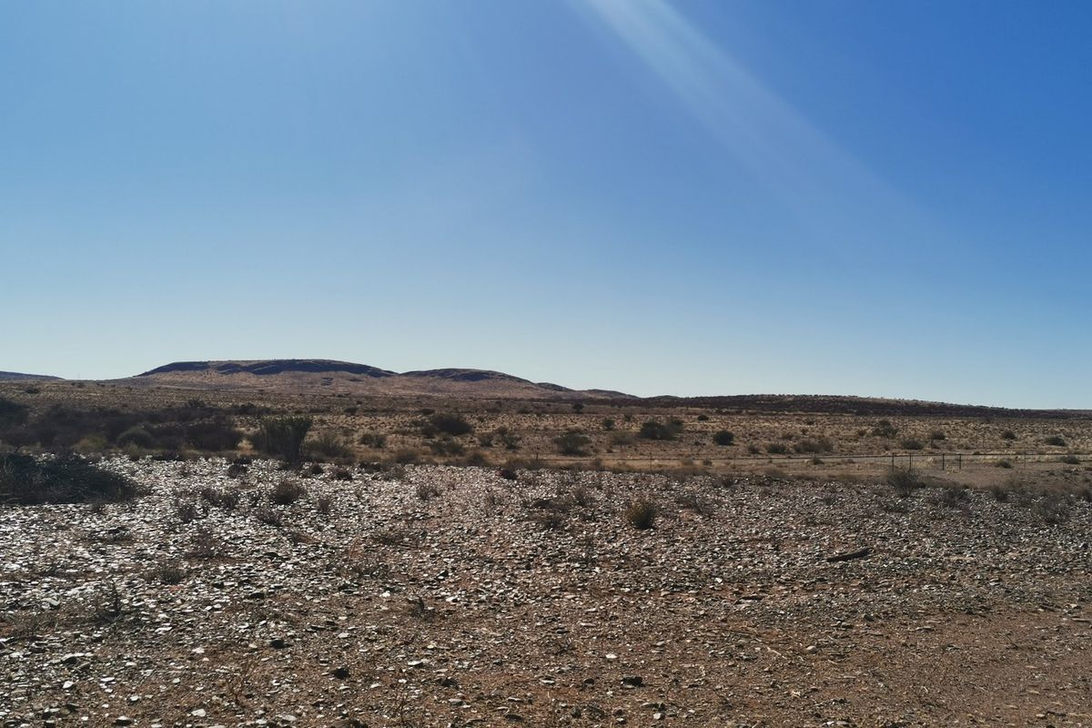 A wide-angle view of the vacant residential land featuring natural arid terrain, rocky ground cover, and distant hills under a clear blue sky.