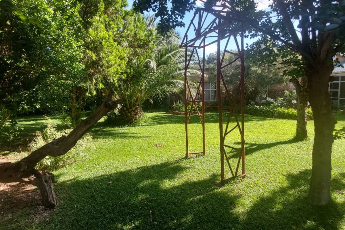 A lush, green garden featuring mature trees, a well-maintained lawn, and a decorative metal garden arch.