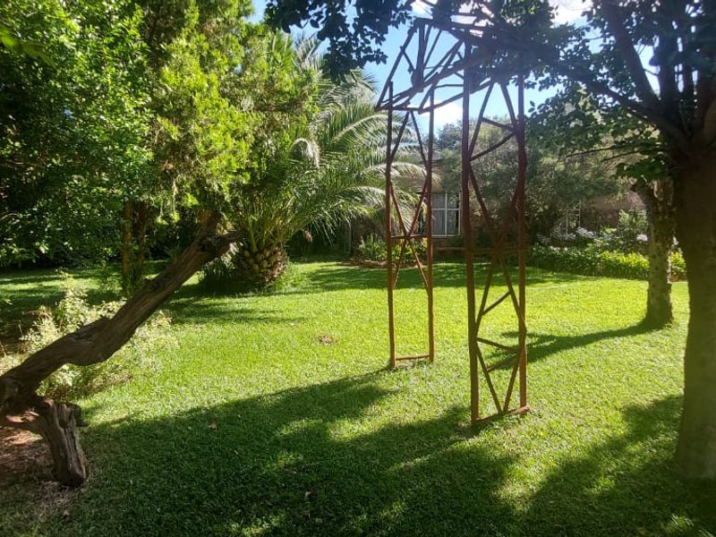 A lush, green garden featuring mature trees, a well-maintained lawn, and a decorative metal garden arch.