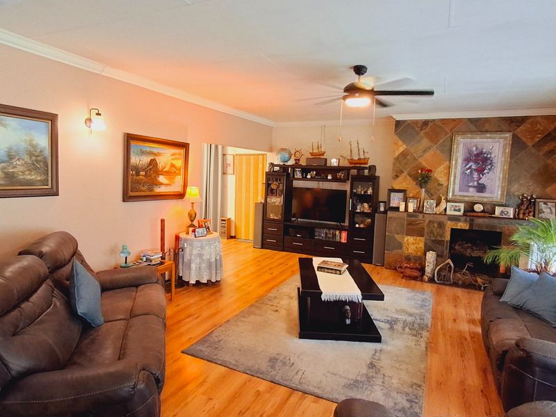 Spacious living room featuring hardwood flooring, a stone-clad fireplace, and a ceiling fan, offering a comfortable and traditional living space.