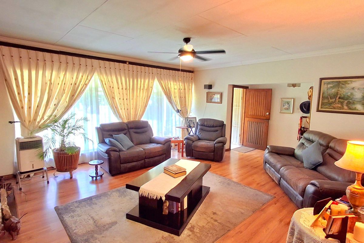 Spacious living room featuring laminate flooring, a ceiling fan, and large windows with curtains, providing a comfortable and well-lit area.