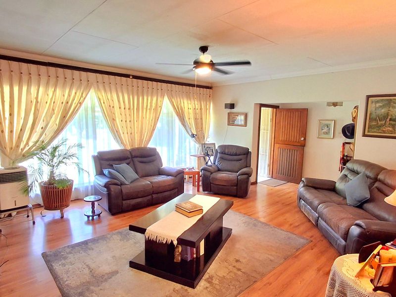 Spacious living room featuring laminate flooring, a ceiling fan, and large windows with curtains, providing a comfortable and well-lit area.