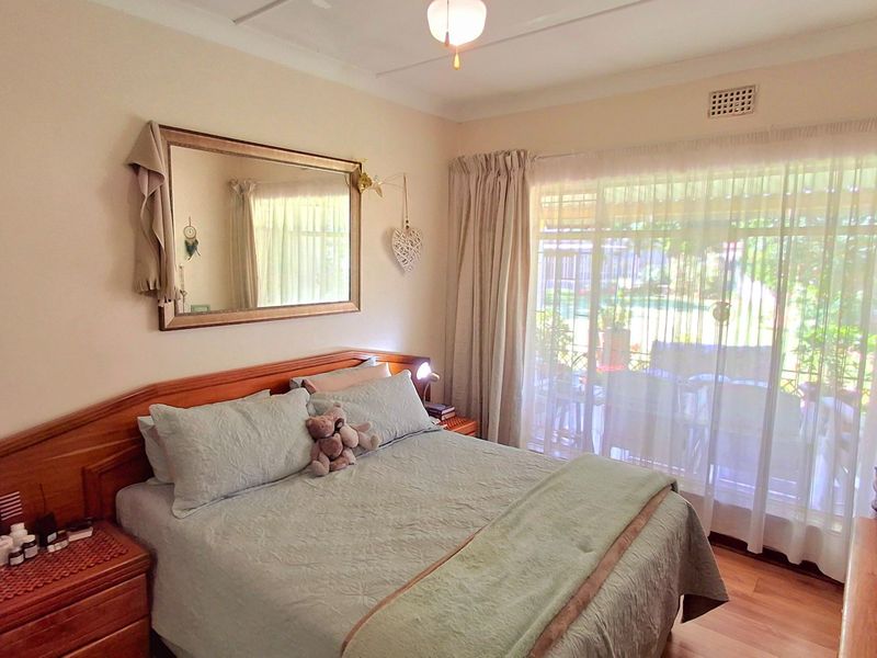 A well-lit bedroom featuring laminate flooring, neutral walls, and a large sliding glass door providing access to the outdoor area.