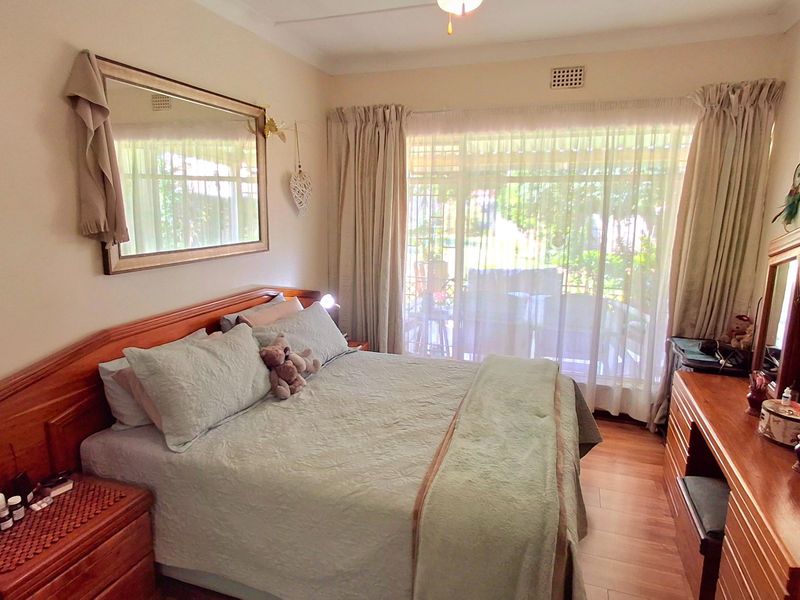 A cozy bedroom featuring laminate flooring, a ceiling fan, and a large sliding glass door providing natural light and access to the outdoor area.