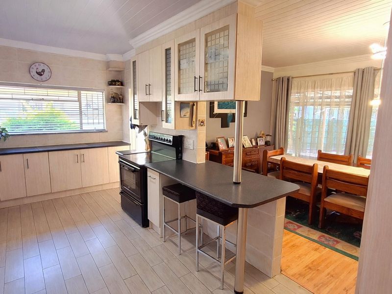 Open-plan kitchen and dining area featuring light-toned cabinetry, a breakfast bar, tiled flooring, and a timber-paneled ceiling.