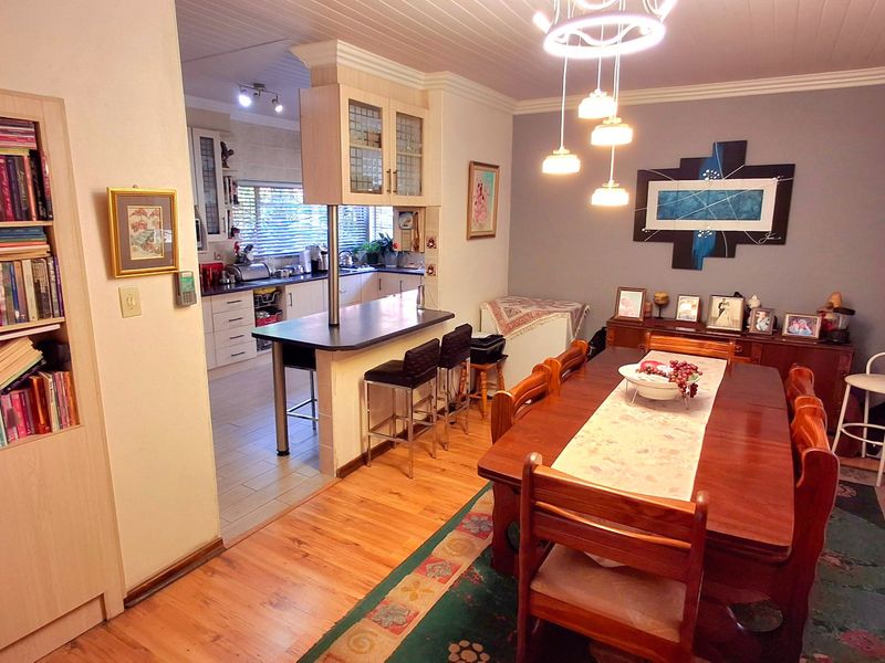 Open-plan dining area featuring laminate flooring and built-in shelving, seamlessly connected to a functional kitchen with a breakfast bar island.