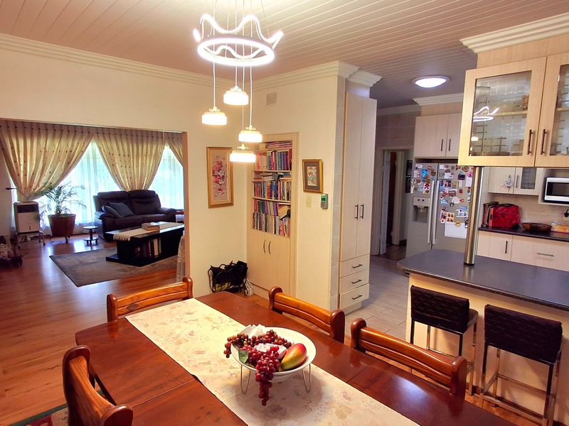 Open-plan living and dining area featuring timber flooring, built-in cabinetry, a breakfast bar, and integrated shelving, creating a functional and connected family space.