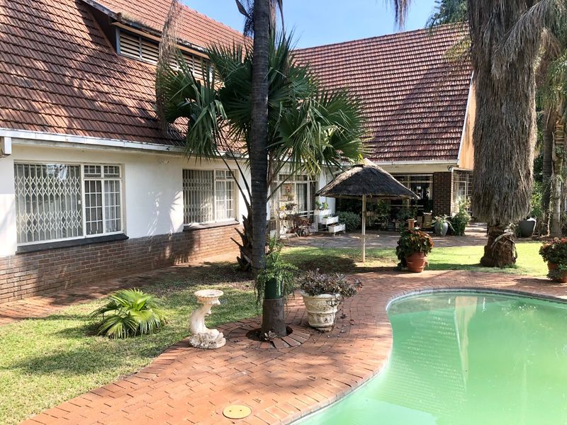 Rear exterior view of the house featuring a swimming pool, brick paved patio area, and traditional tiled roof architecture.
