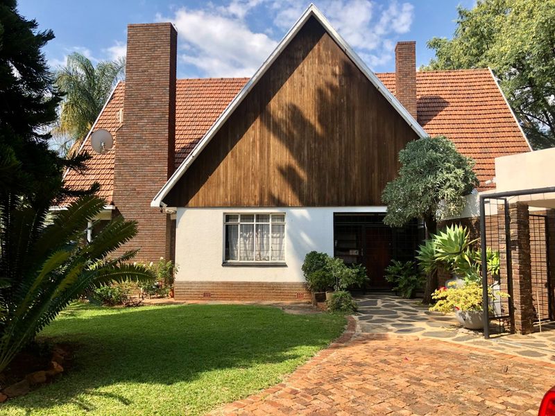 Front elevation of a charming house featuring a steep pitched roof, timber cladding, brick chimneys, and a stone-paved entrance path set within a landscaped garden.