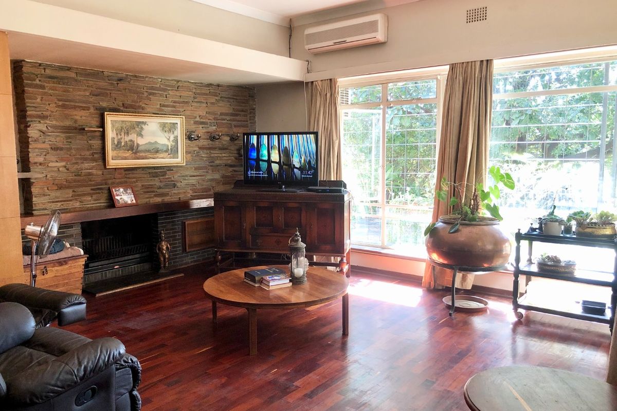 Spacious living room featuring a prominent stone fireplace, rich hardwood flooring, and large windows that provide ample natural light.
