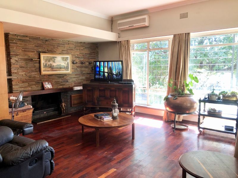 Spacious living room featuring a prominent stone fireplace, rich hardwood flooring, and large windows that provide ample natural light.