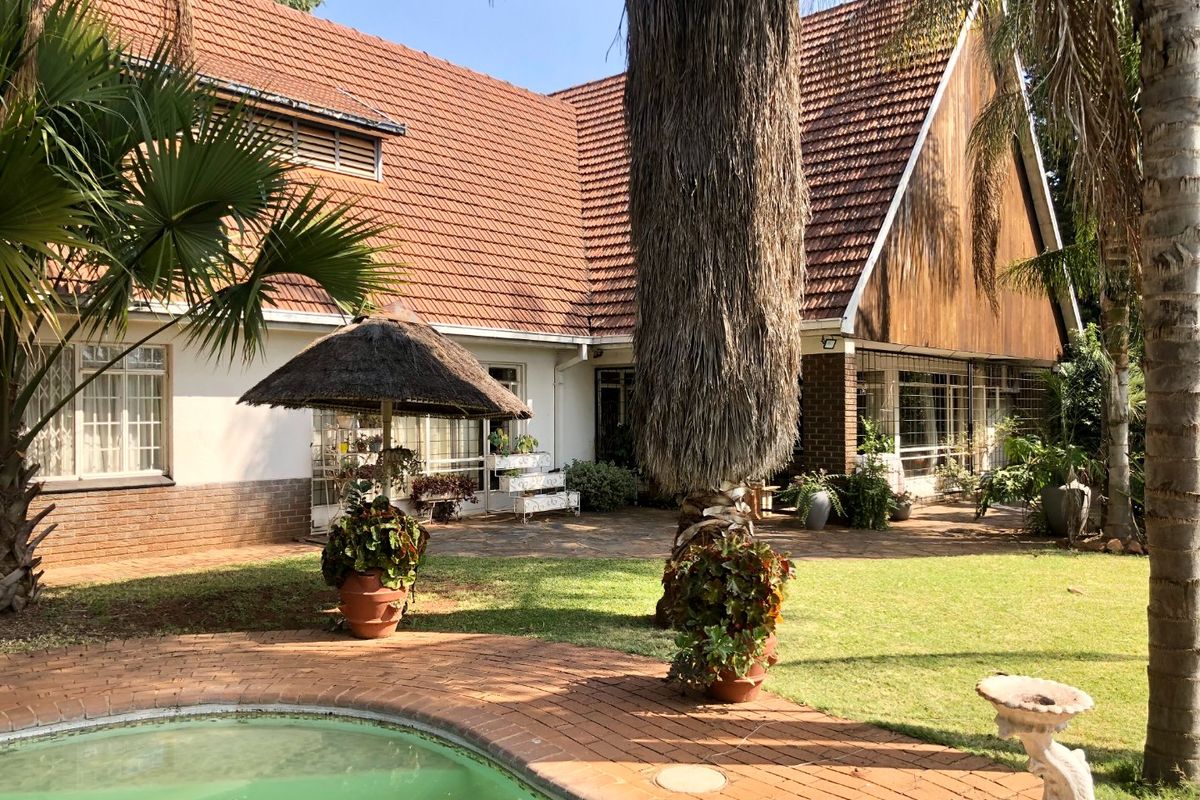 Rear view of the property featuring a swimming pool, brick paved patio area, and a house with a tiled roof and timber cladding accents.