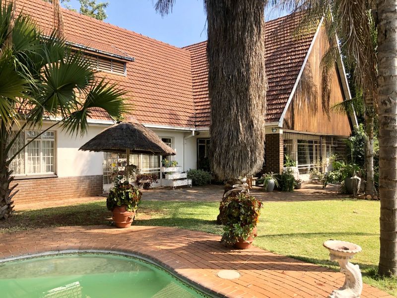 Rear view of the property featuring a swimming pool, brick paved patio area, and a house with a tiled roof and timber cladding accents.