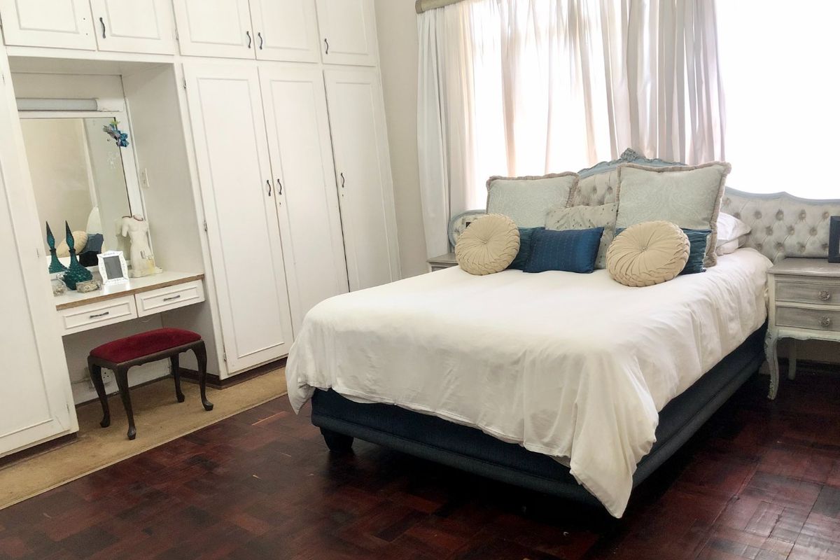 Spacious bedroom featuring classic parquet flooring, extensive built-in cabinetry with an integrated vanity, and large windows with curtain rails.