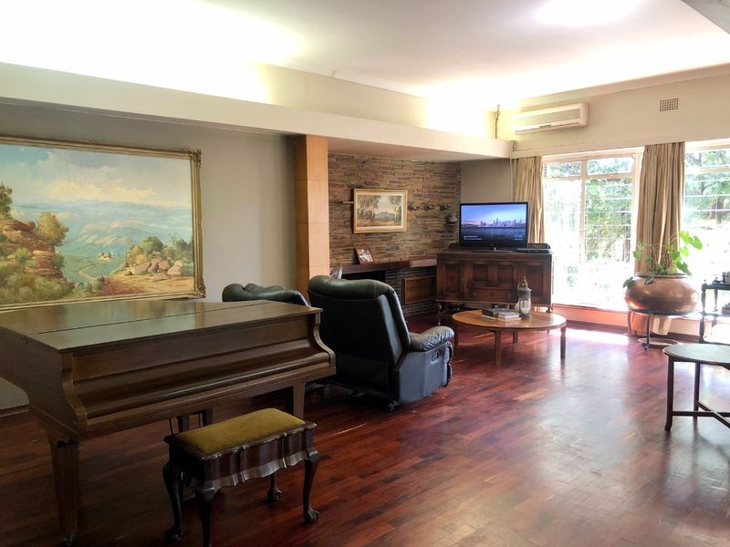 Spacious living room featuring polished hardwood flooring, a stone feature wall, and large windows providing natural light and garden views.