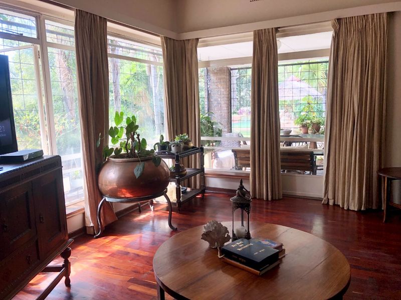 A bright living room featuring polished hardwood flooring and expansive windows that provide natural light and views of the outdoor patio area.