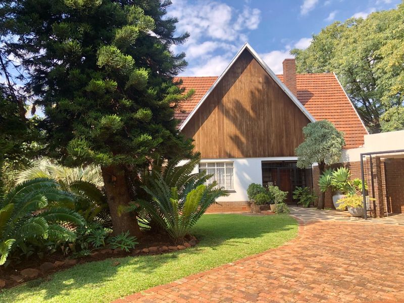 Front view of a charming house featuring a brick driveway, mature garden, and distinctive timber-clad gable roof design.
