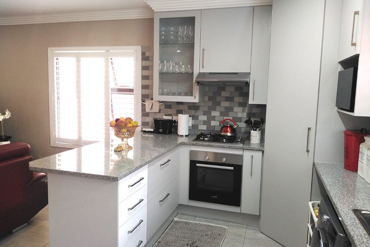 Modern kitchen featuring light grey cabinetry, granite countertops, built-in oven, gas hob, and stylish tiled splashback, complemented by plantation shutters.