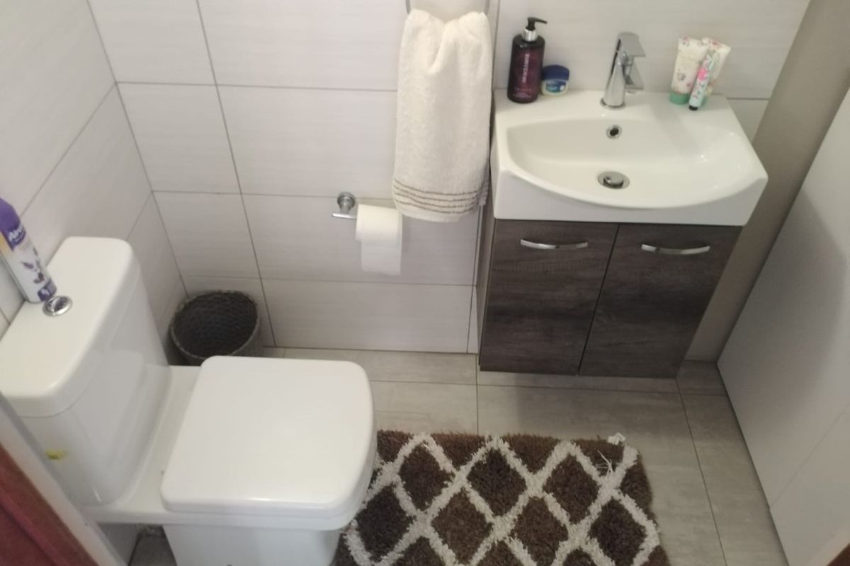 A compact, modern bathroom featuring a wall-mounted vanity with a ceramic basin, chrome mixer tap, and a white toilet suite with tiled finishes.