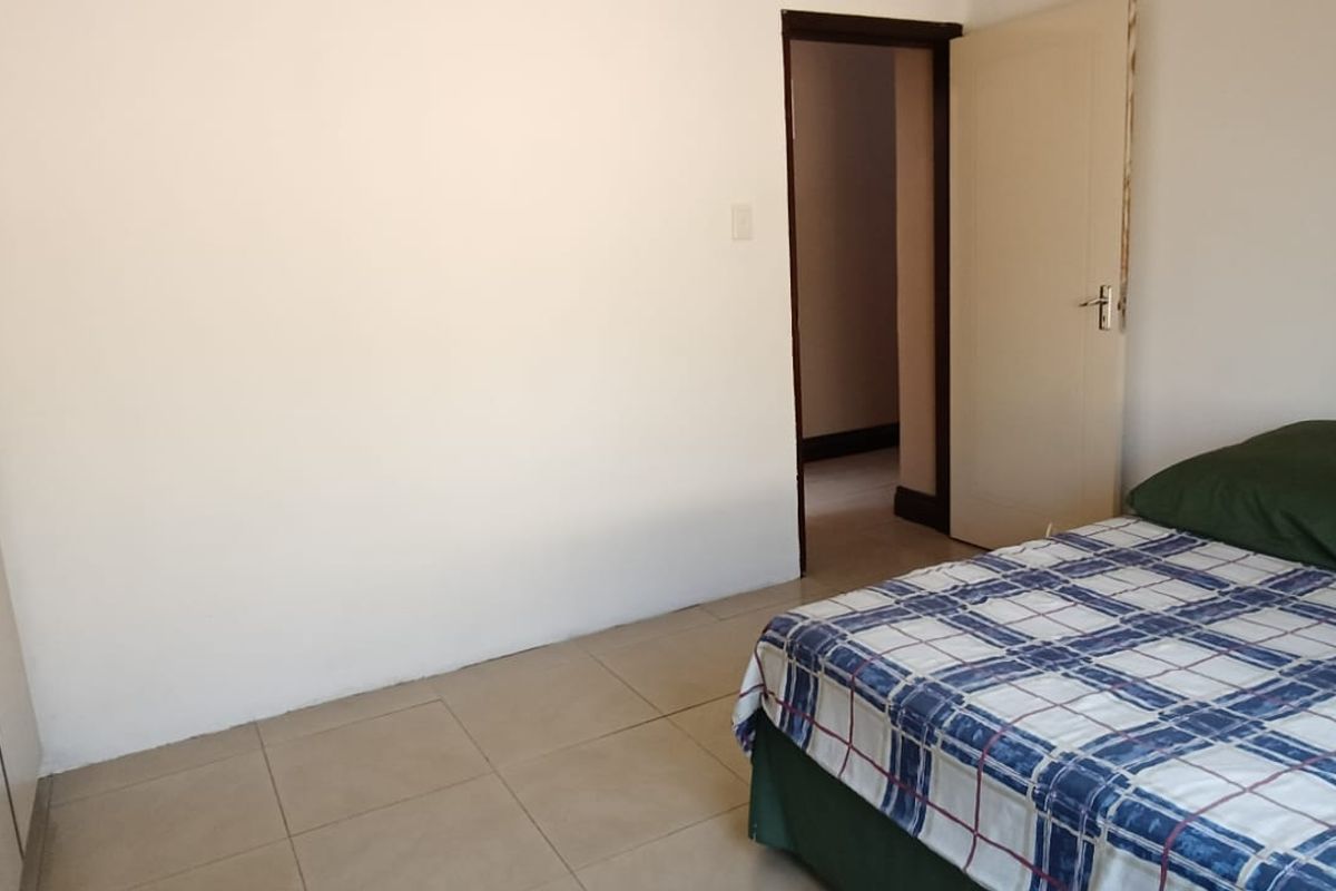 A simple bedroom featuring tiled flooring and a built-in wardrobe, providing a functional and neutral living space.