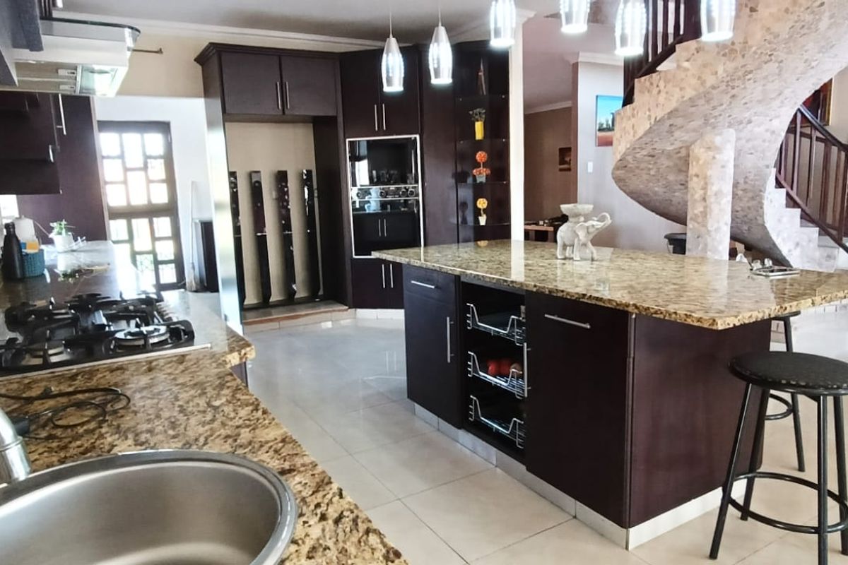 Spacious kitchen featuring dark cabinetry, granite countertops, a central island, and a striking spiral staircase, creating an open-plan flow.