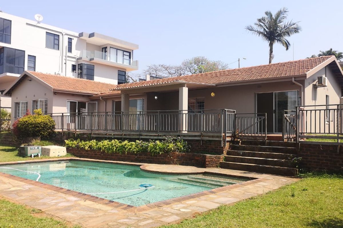 Rear view of the property featuring a swimming pool, raised patio with metal balustrade, and direct access to the home via sliding glass doors.