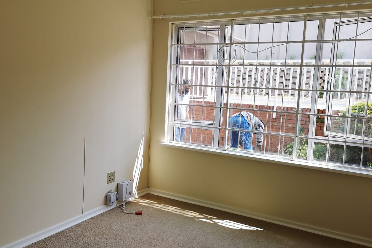 An empty bedroom featuring carpet flooring and security bars on the window, requiring minor cosmetic updates.
