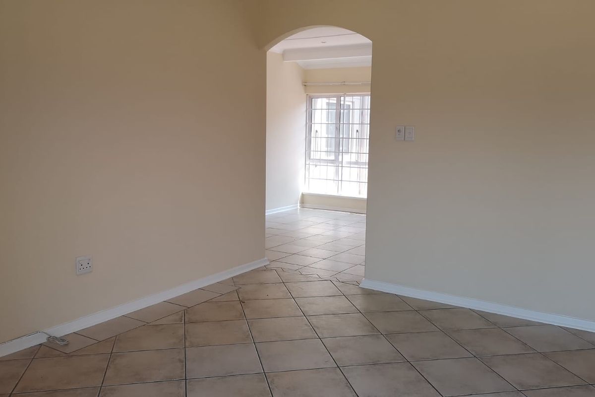 An empty living area featuring neutral walls, tiled flooring, and an arched transition to an adjacent room with security-barred windows.