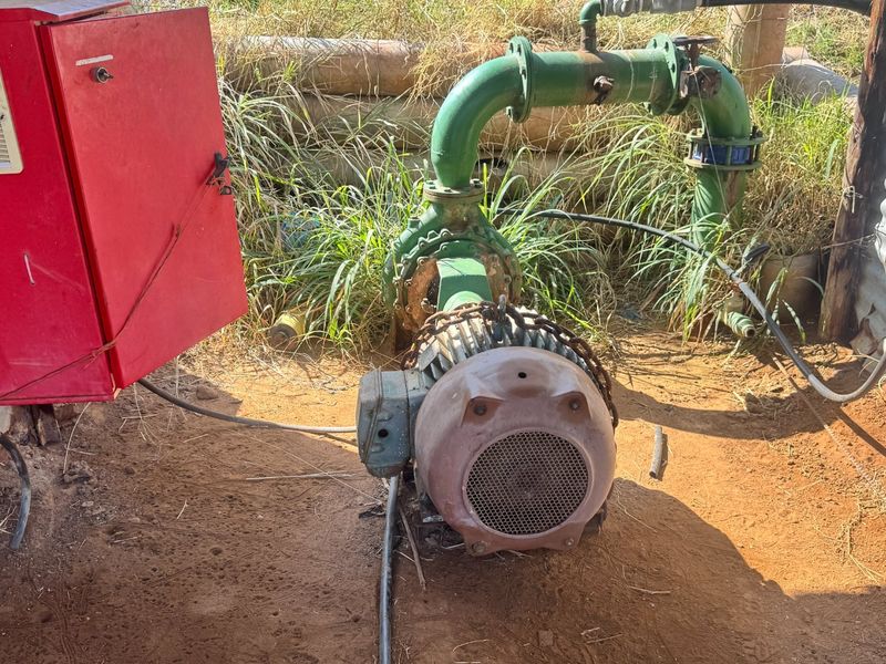 Outdoor utility area featuring an electric water pump system with associated piping and electrical control housing on a farm property.