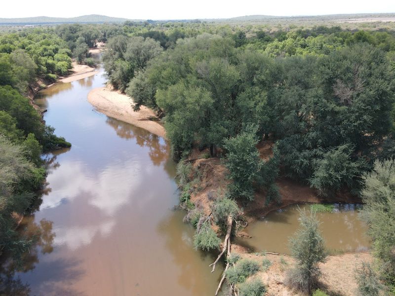 Aerial view of a natural river flowing through the farm landscape, surrounded by dense indigenous trees and vegetation.