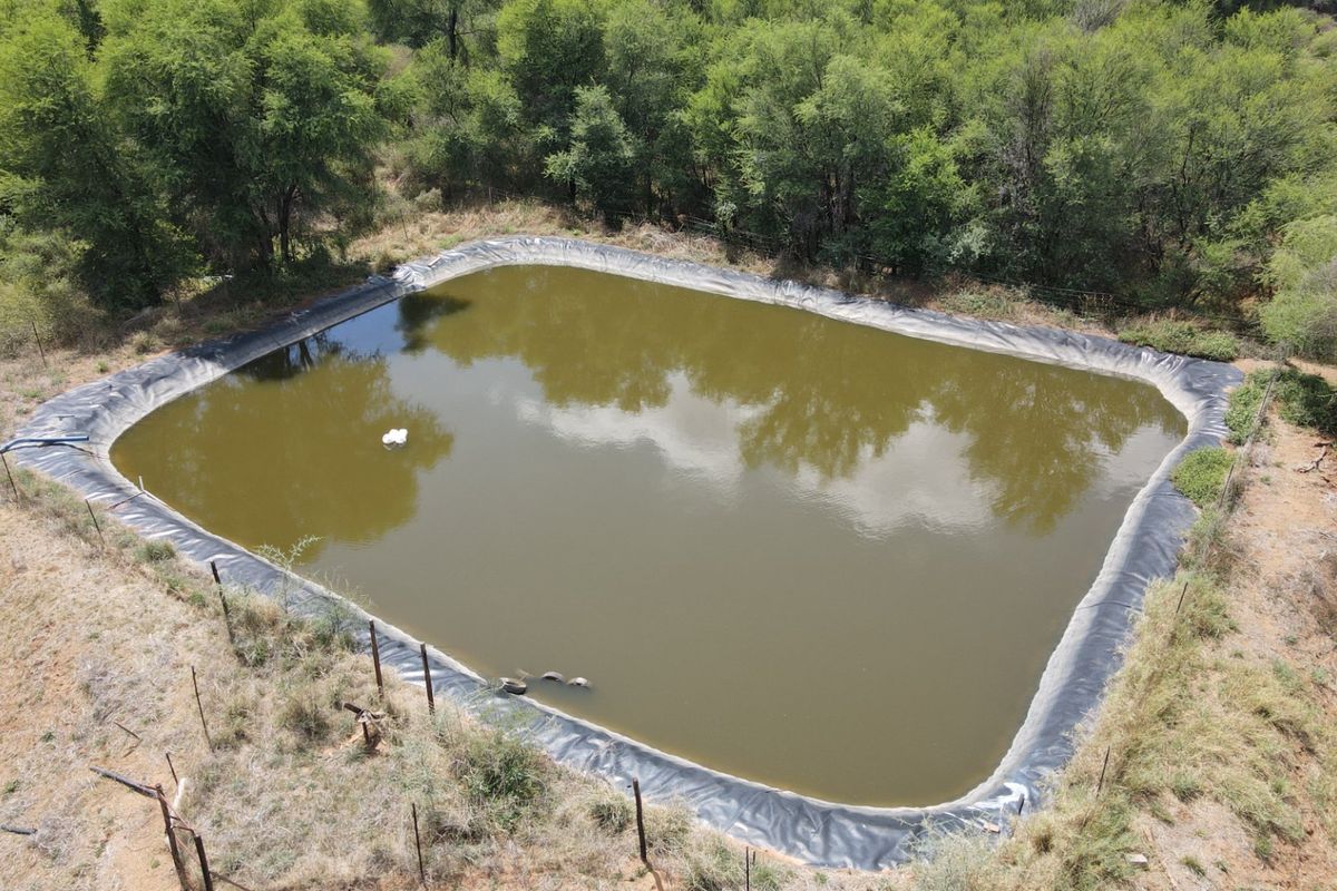 An aerial view of a large, lined farm reservoir or dam surrounded by natural vegetation and perimeter fencing.