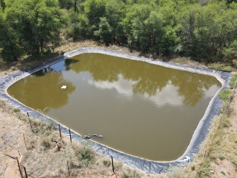 An aerial view of a large, lined farm reservoir or dam surrounded by natural vegetation and perimeter fencing.