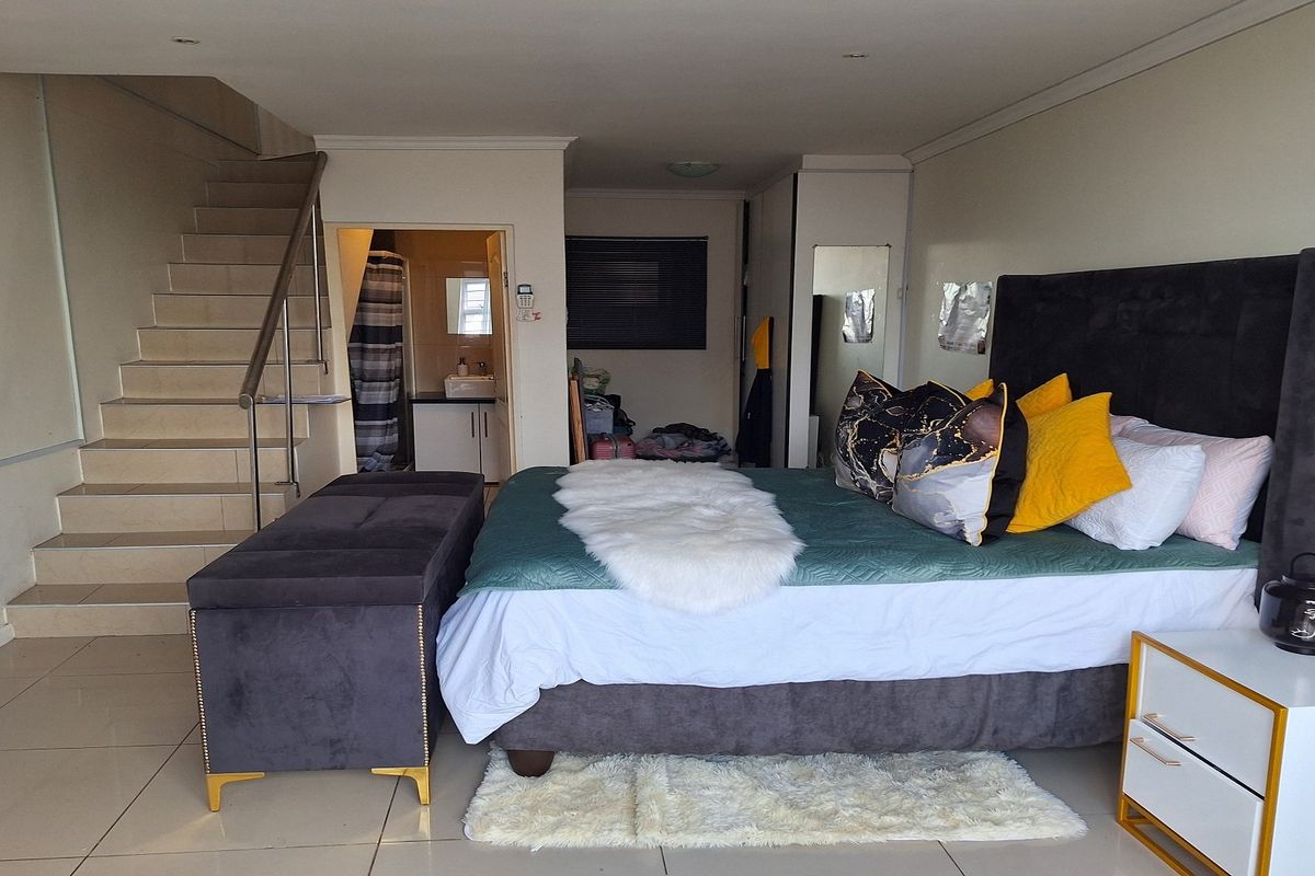 Spacious bedroom featuring tiled flooring, a built-in staircase leading to an upper level, and integrated storage cupboards with an adjacent en-suite bathroom.