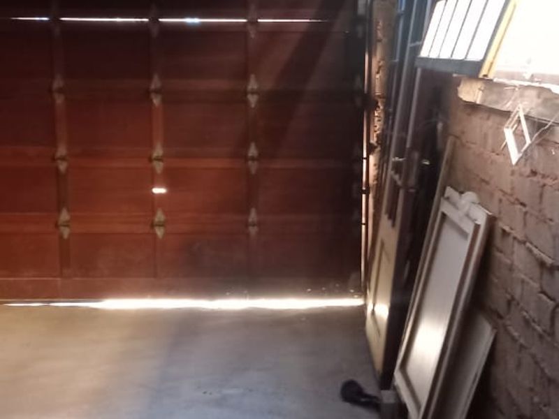 A basic garage space featuring a sectional wooden door, concrete flooring, and exposed brick walls with an open-truss corrugated metal roof.