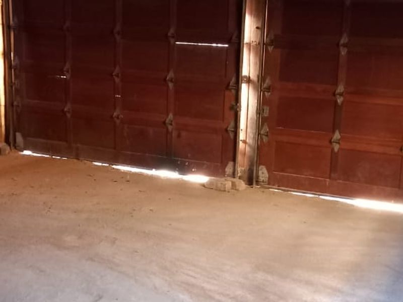 A functional garage space featuring dual sectional timber doors, exposed roof rafters, and a concrete floor, offering ample storage or parking potential.