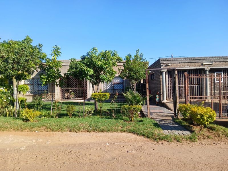 Front view of a residential property featuring a landscaped garden, paved walkway, and secure metal gates and window bars.
