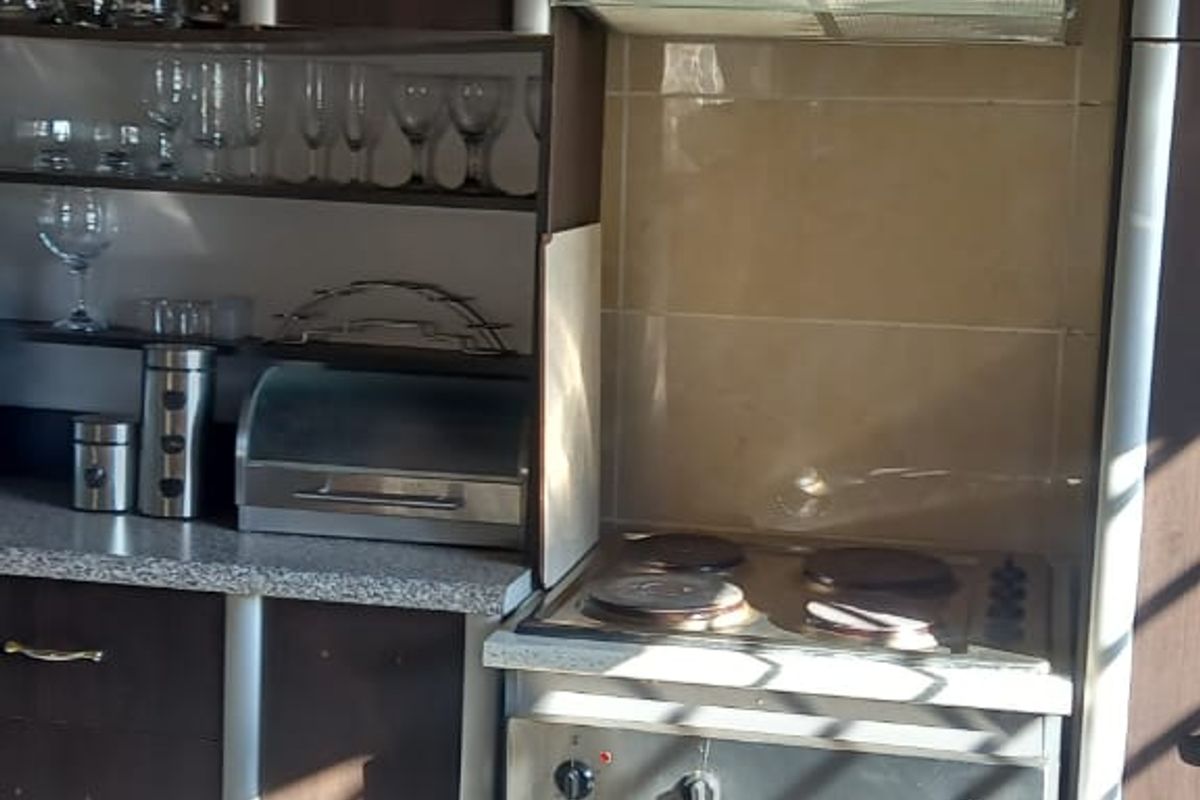 Compact kitchen area featuring built-in cabinetry, an electric stove with oven, extractor fan, and tiled splashback, requiring some cosmetic maintenance.