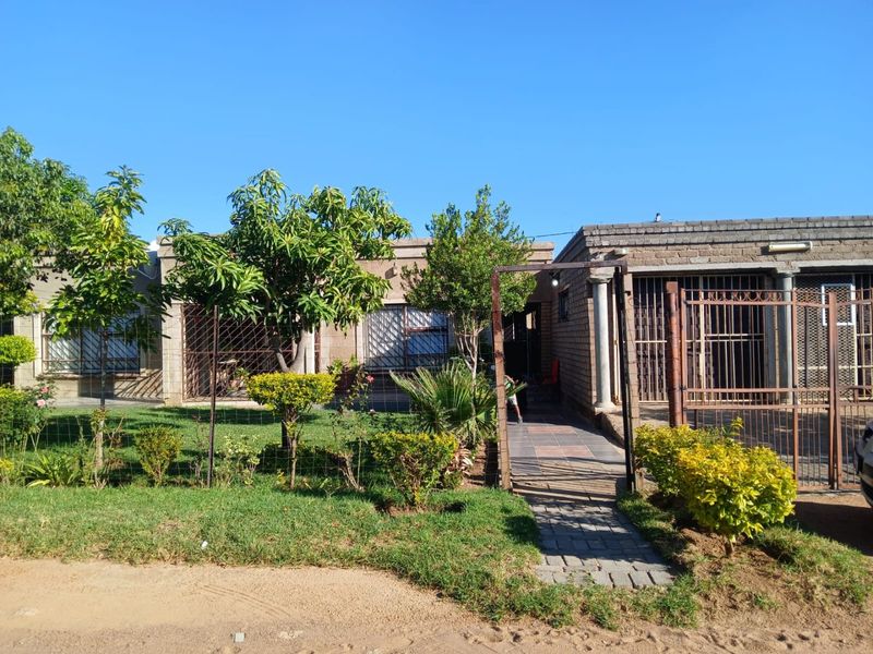 Front view of a single-story brick house featuring a paved walkway, security gates, and established garden area.