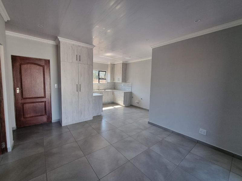 An open-plan living and kitchen area featuring modern grey floor tiles, neutral walls, and built-in cabinetry, offering a clean and versatile living space.