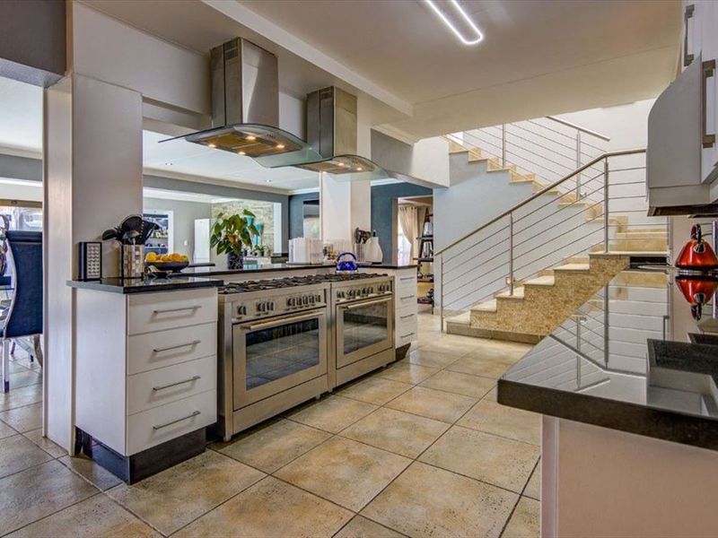 Modern kitchen featuring stainless steel double ovens, extractor fans, granite countertops, and tiled flooring, seamlessly integrated with an open-plan staircase.